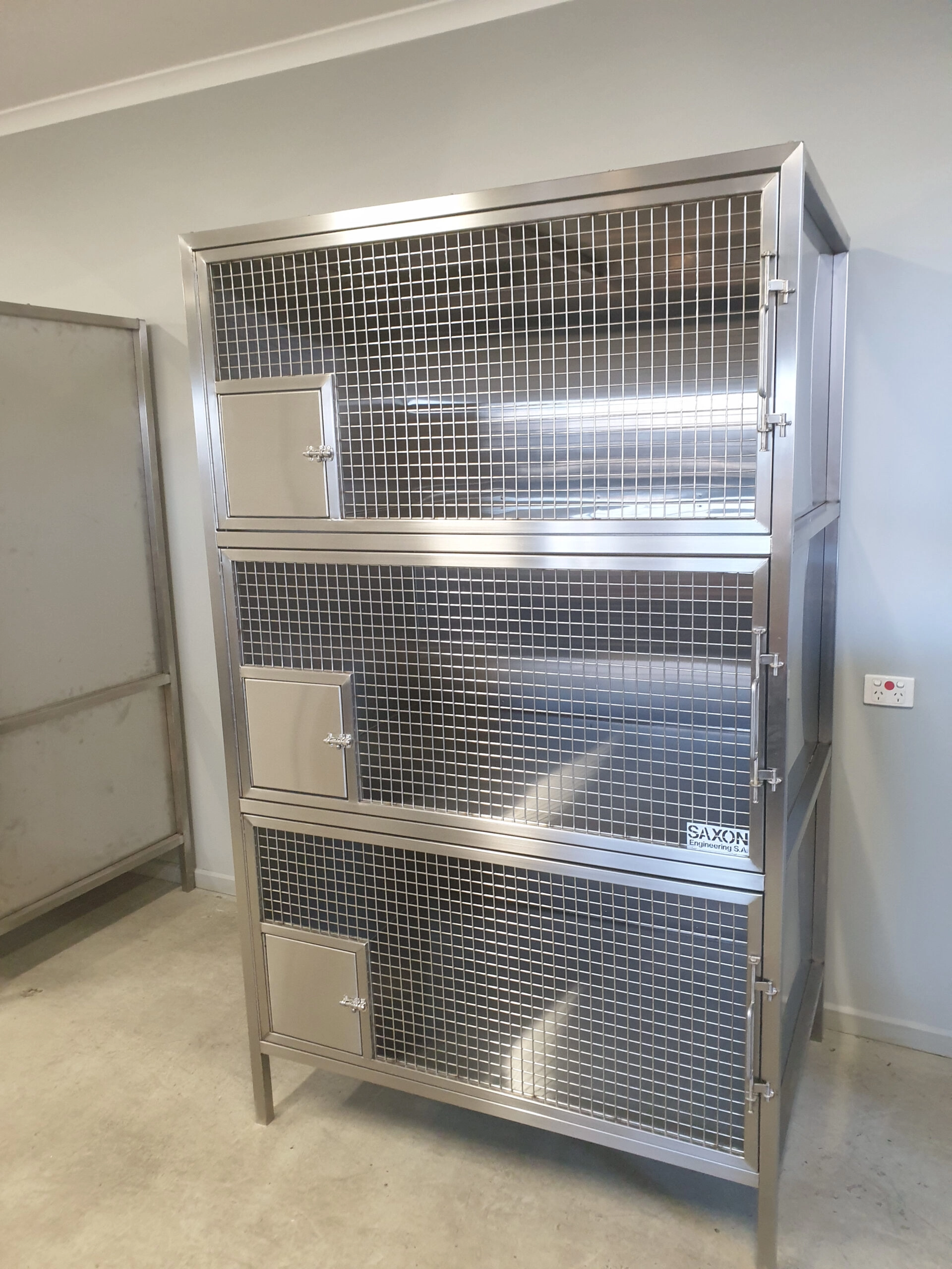 Stainless steel fabrication: vet cages. 1 unit with 3 sections vertically stacked each front is a large door with mesh front and small square sheet metal door in the bottom left corner. Each door is securely locked. The rest of the cage is sheet metal all 2B finish 316 stainless steel.